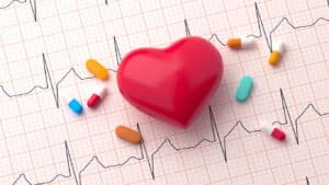 a 3D heart placed on an EKG printout, surrounded by various medications for atrial fibrillation